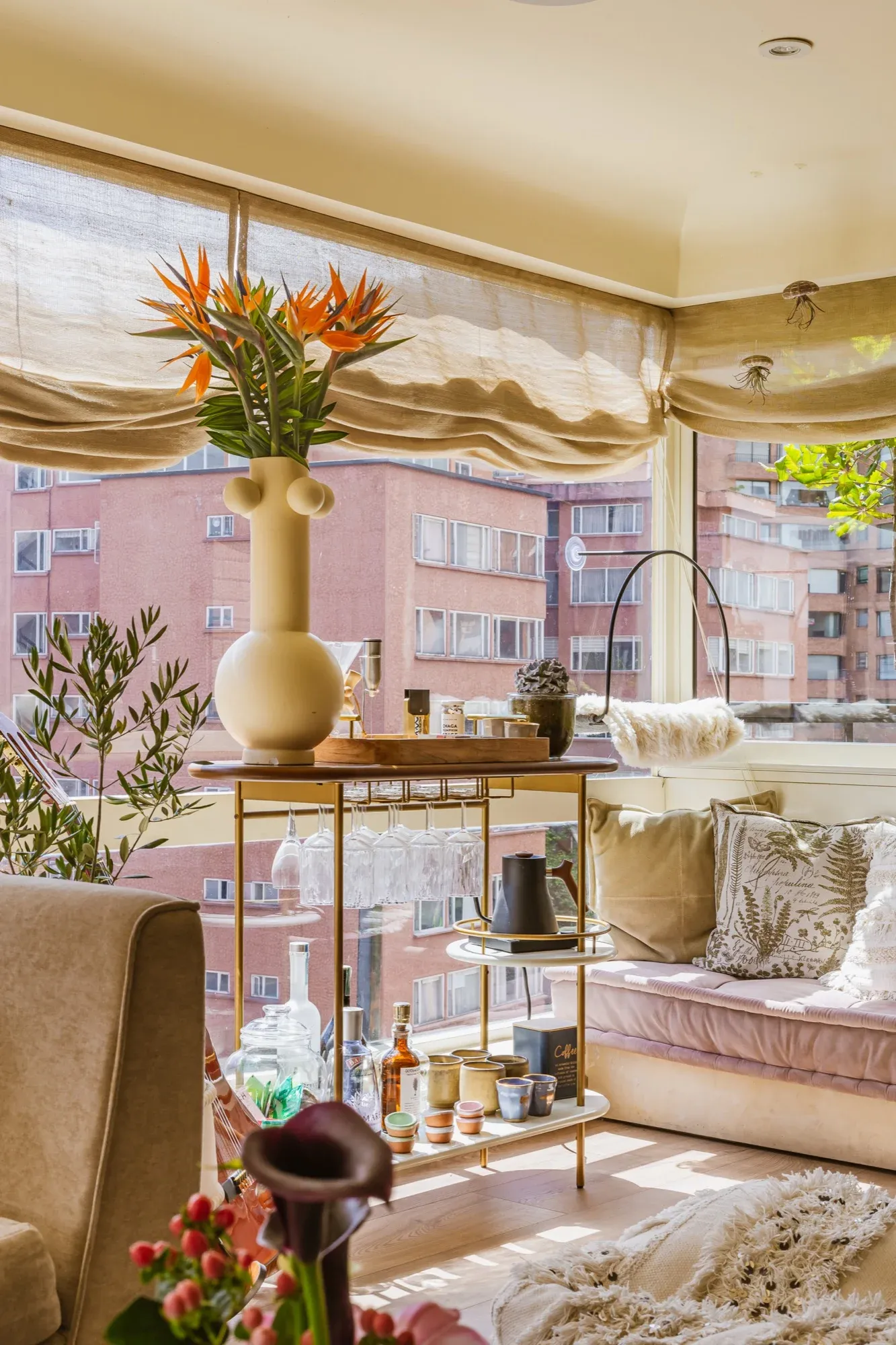 Rincón de una sala con carrito bar, flores y vista a la ciudad