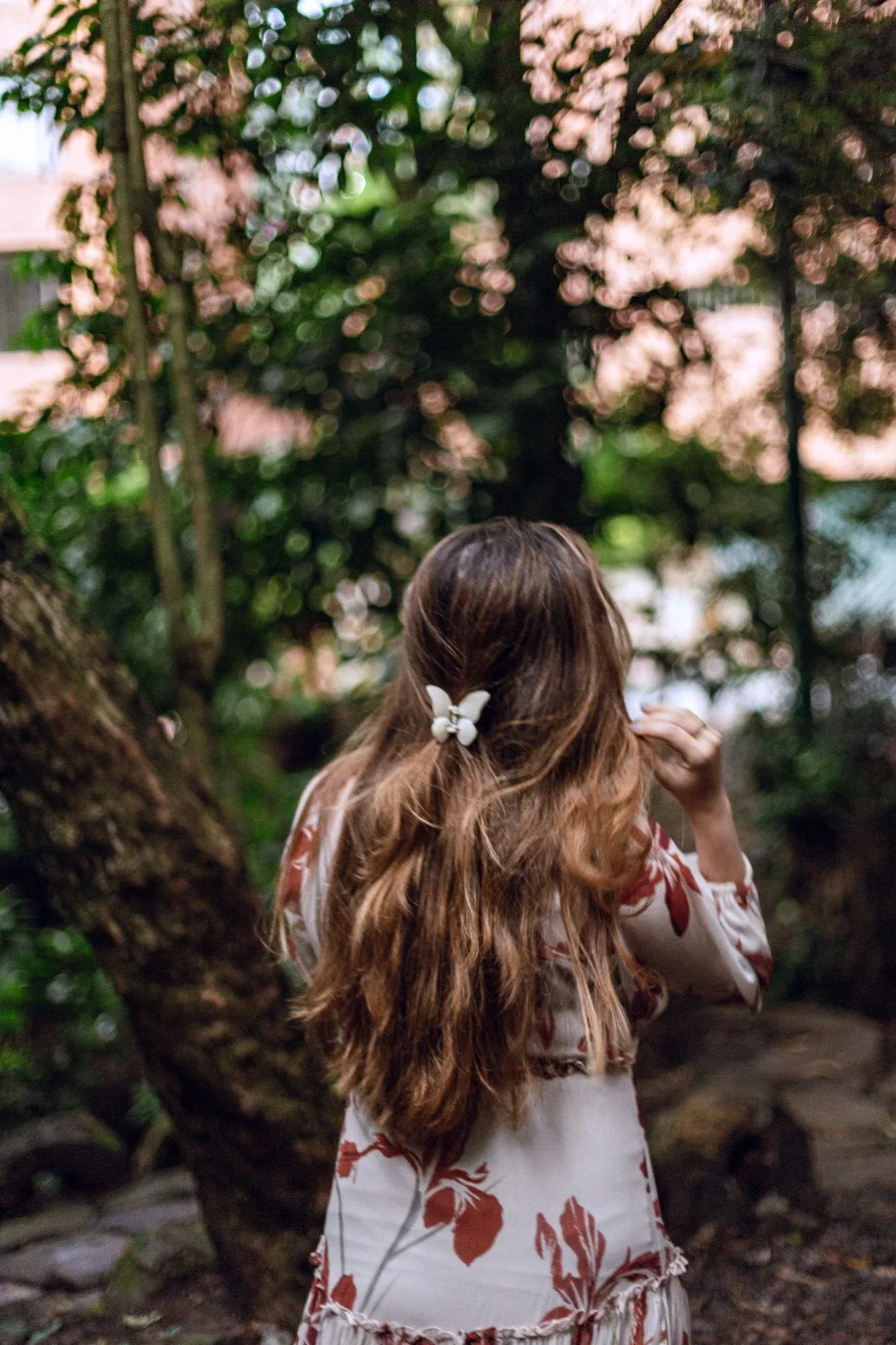 Mujer de espaldas entre árboles, con el cabello suelto y un broche de mariposa
