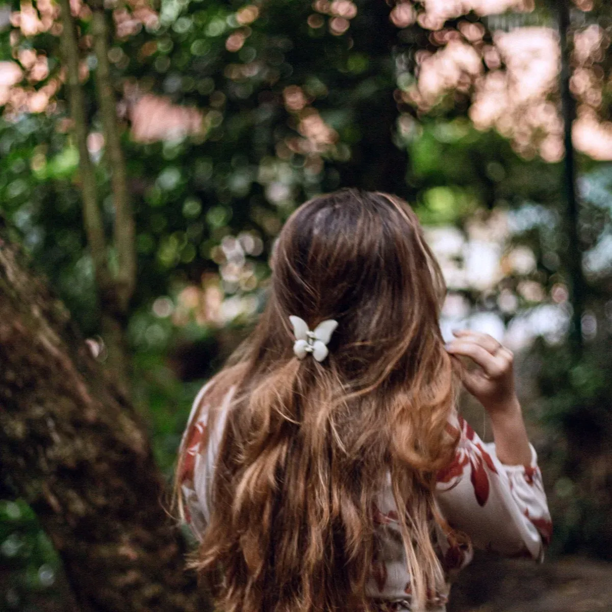 Mujer de espaldas caminando entre árboles, con un broche de mariposa sosteniendo su cabello